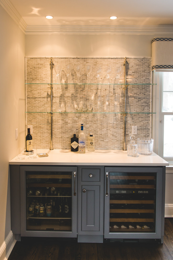 Photo of a small transitional single-wall wet bar in New York with no sink, recessed-panel cabinets, grey cabinets, solid surface benchtops, grey splashback, mosaic tile splashback and dark hardwood floors.