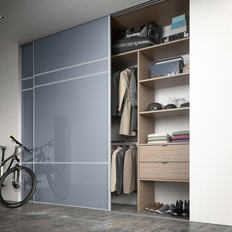 This is an example of a large contemporary gender-neutral built-in wardrobe in Hertfordshire with glass-front cabinets, light wood cabinets and concrete floors.