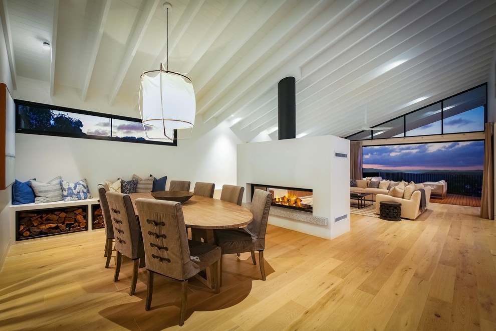 This is an example of a contemporary open plan dining in Wollongong with white walls, medium hardwood floors, a two-sided fireplace and brown floor.