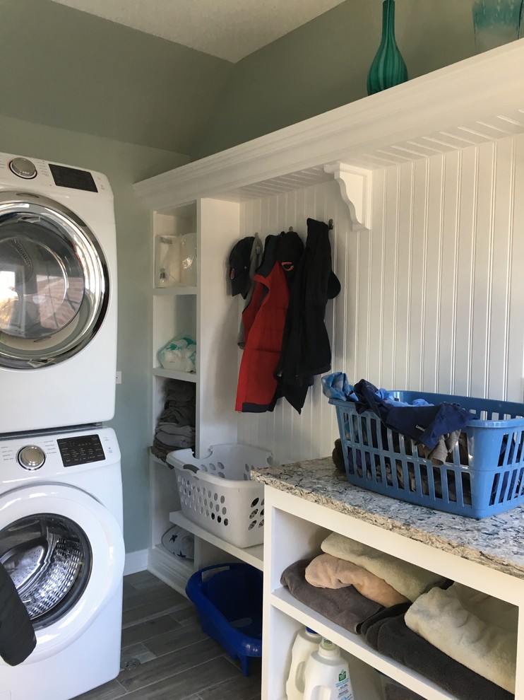 Inspiration for a mid-sized transitional single-wall dedicated laundry room in Chicago with open cabinets, white cabinets, quartz benchtops, green walls, porcelain floors, a stacked washer and dryer, grey floor and grey benchtop.