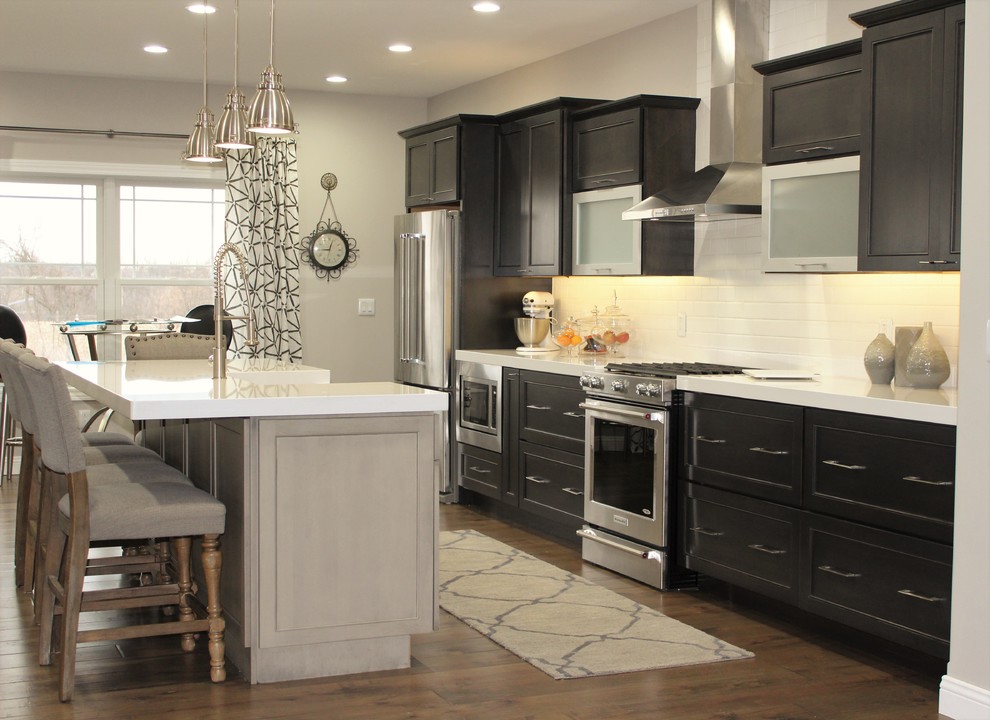Mid-sized transitional galley medium tone wood floor eat-in kitchen photo in Chicago with a farmhouse sink, recessed-panel cabinets, gray cabinets, quartzite countertops, white backsplash, ceramic backsplash, stainless steel appliances and an island