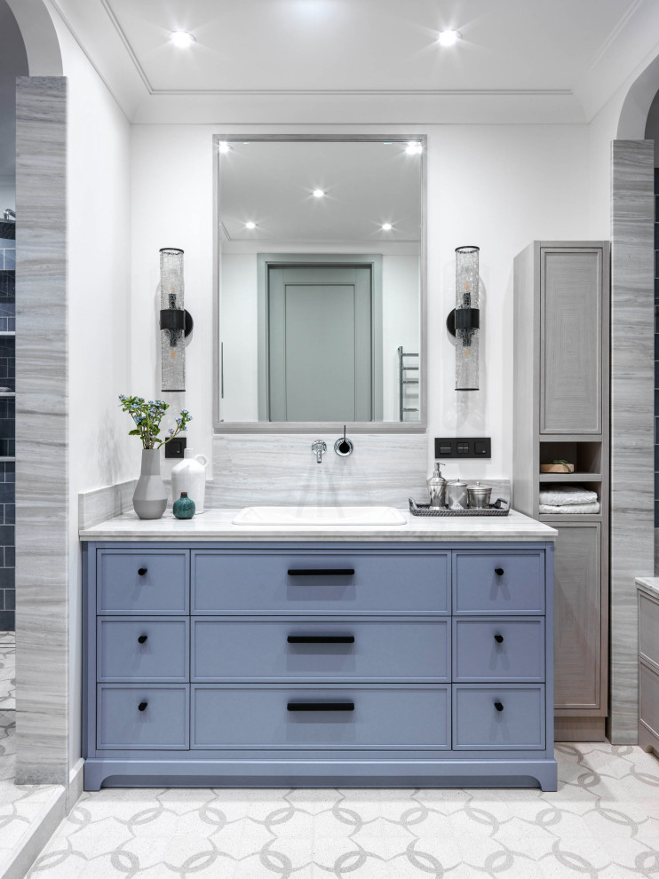 This is an example of a mid-sized contemporary master bathroom in Moscow with recessed-panel cabinets, blue cabinets, white walls, cement tiles, a drop-in sink, marble benchtops, white floor, grey benchtops and gray tile.