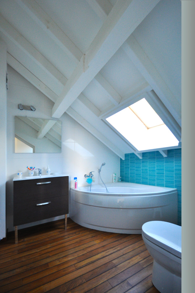 This is an example of a small contemporary kids bathroom in Grenoble with a corner tub, a one-piece toilet, blue walls, dark hardwood floors, a console sink and solid surface benchtops.