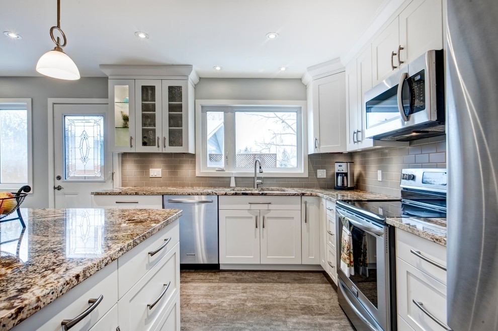 Mid-sized transitional l-shaped vinyl floor eat-in kitchen photo in Calgary with an undermount sink, shaker cabinets, white cabinets, granite countertops, gray backsplash, subway tile backsplash, stainless steel appliances and an island