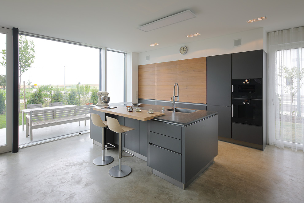 Design ideas for a mid-sized contemporary galley open plan kitchen in Munich with a drop-in sink, flat-panel cabinets, grey cabinets, black appliances, vinyl floors, with island, beige floor and grey benchtop.