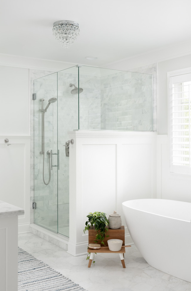 This is an example of a mid-sized transitional master bathroom in Chicago with recessed-panel cabinets, white cabinets, a freestanding tub, a corner shower, a one-piece toilet, gray tile, marble, grey walls, marble floors, an undermount sink, marble benchtops, grey floor, a hinged shower door, grey benchtops, a niche, a double vanity, a built-in vanity and decorative wall panelling.
