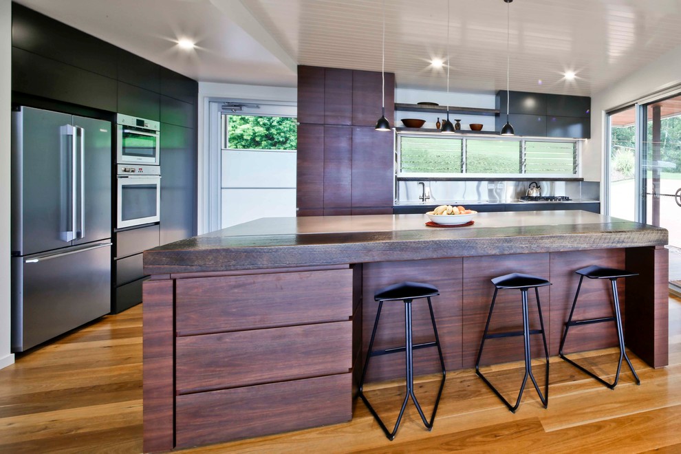 Photo of a mid-sized modern eat-in kitchen in Gold Coast - Tweed with flat-panel cabinets, dark wood cabinets, wood benchtops, metallic splashback, metal splashback, stainless steel appliances, medium hardwood floors and with island.