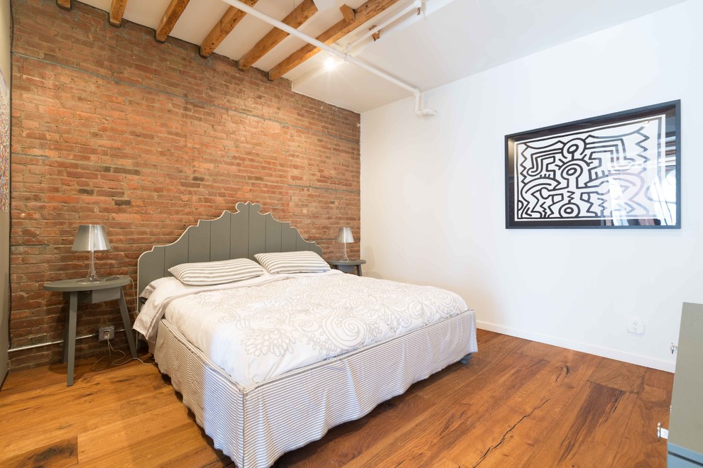 Photo of an industrial bedroom in New York with white walls, medium hardwood floors and brown floor.