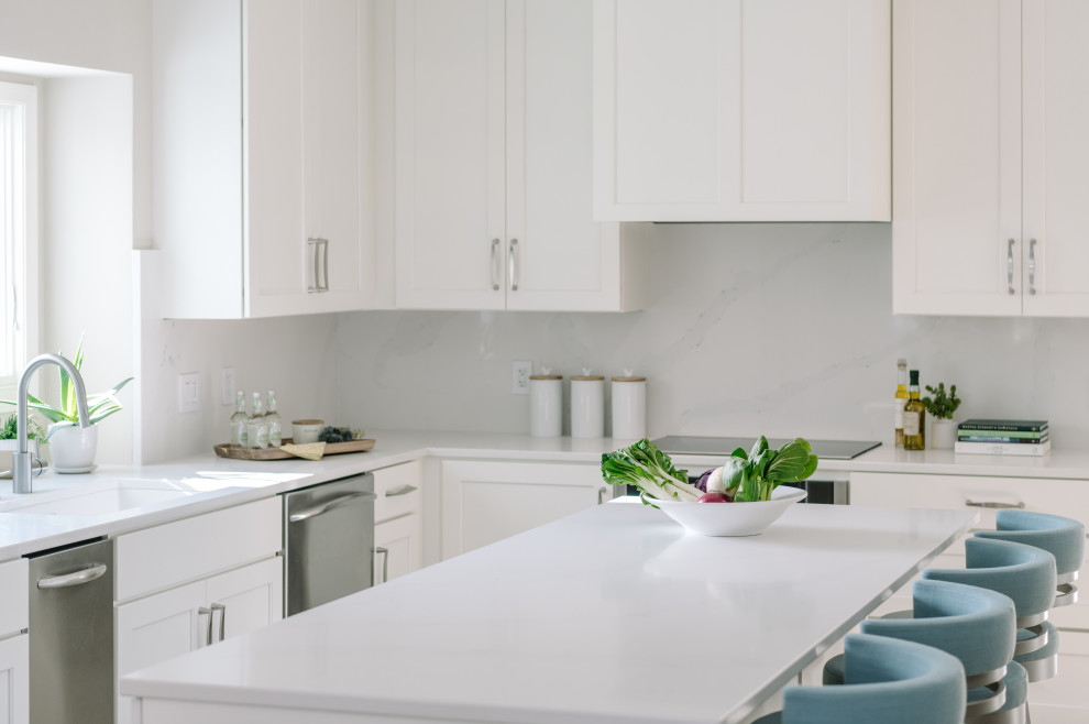 Klassisk inredning av ett stort vit vitt kök, med en undermonterad diskho, skåp i shakerstil, vita skåp, bänkskiva i kvarts, vitt stänkskydd, rostfria vitvaror, laminatgolv, en köksö och brunt golv