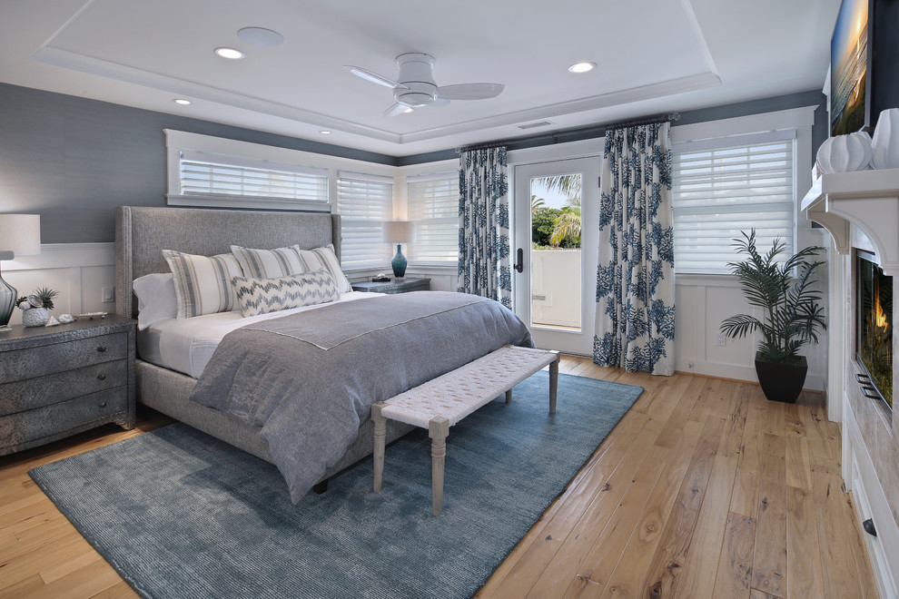 Photo of a mid-sized beach style master bedroom in San Diego with blue walls, light hardwood floors, a standard fireplace and a tile fireplace surround.