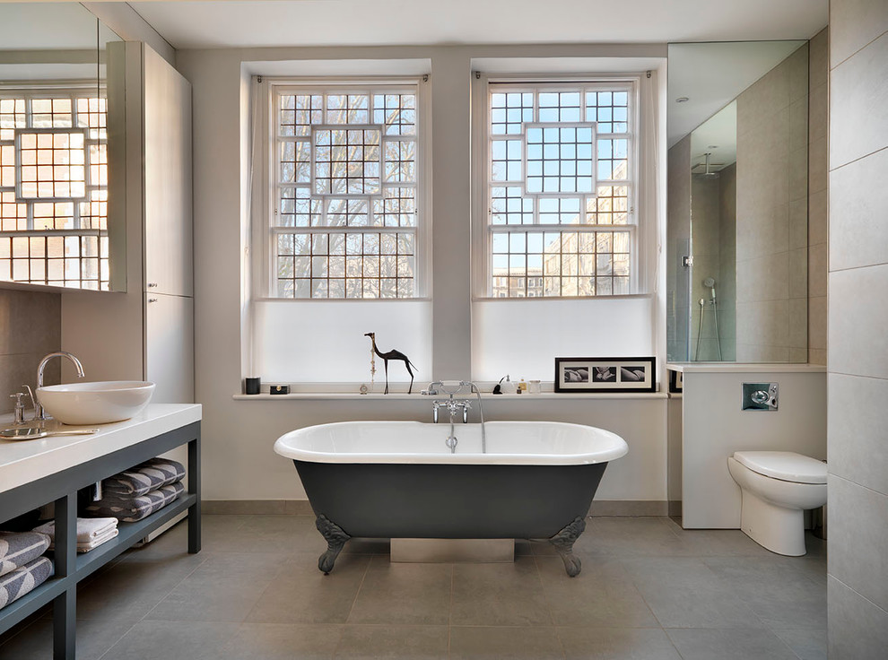 Design ideas for a large contemporary master bathroom in London with a console sink, flat-panel cabinets, white cabinets, marble benchtops, a claw-foot tub, a one-piece toilet, beige tile, porcelain tile, white walls and porcelain floors.