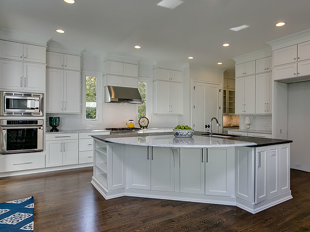 Example of a large transitional l-shaped medium tone wood floor and brown floor open concept kitchen design in Raleigh with an undermount sink, recessed-panel cabinets, white cabinets, solid surface countertops, white backsplash, glass tile backsplash, stainless steel appliances, an island and white countertops