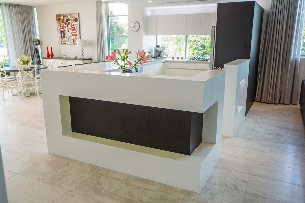 This is an example of a large u-shaped open plan kitchen in Brisbane with a double-bowl sink, recessed-panel cabinets, white cabinets, solid surface benchtops, stainless steel appliances, porcelain floors, multiple islands, brown floor and brown benchtop.