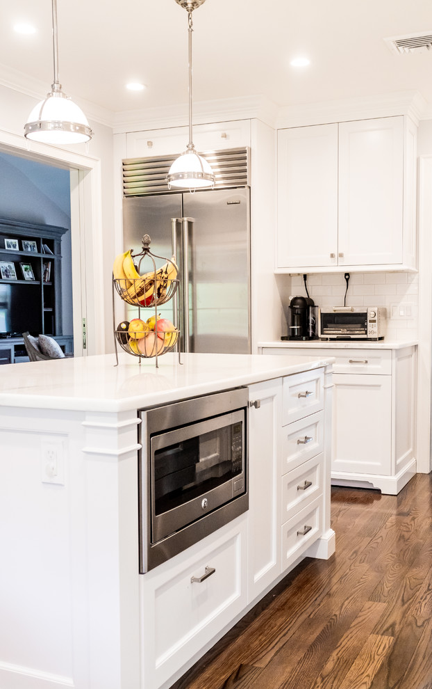 Enclosed kitchen - mid-sized transitional dark wood floor and brown floor enclosed kitchen idea in New York with a farmhouse sink, recessed-panel cabinets, white cabinets, quartzite countertops, white backsplash, subway tile backsplash, stainless steel appliances and an island