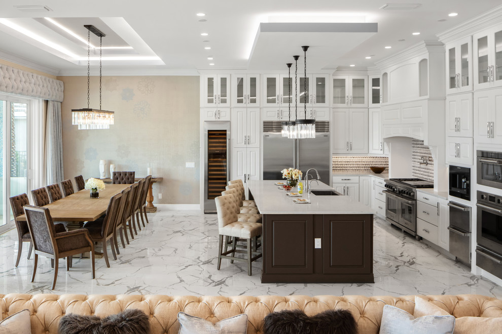 Large contemporary l-shaped open plan kitchen in Orlando with a farmhouse sink, raised-panel cabinets, white cabinets, quartz benchtops, multi-coloured splashback, mosaic tile splashback, stainless steel appliances, porcelain floors, with island, white floor and white benchtop.