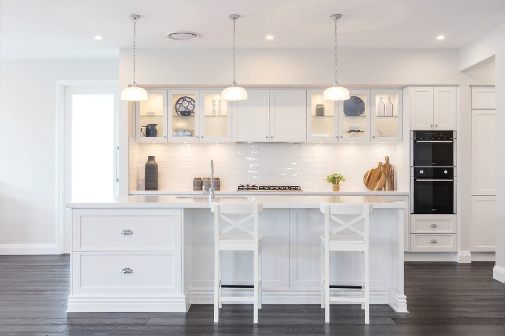 Design ideas for a transitional galley kitchen in Central Coast with shaker cabinets, white cabinets, white splashback, black appliances, with island, grey floor and white benchtop.