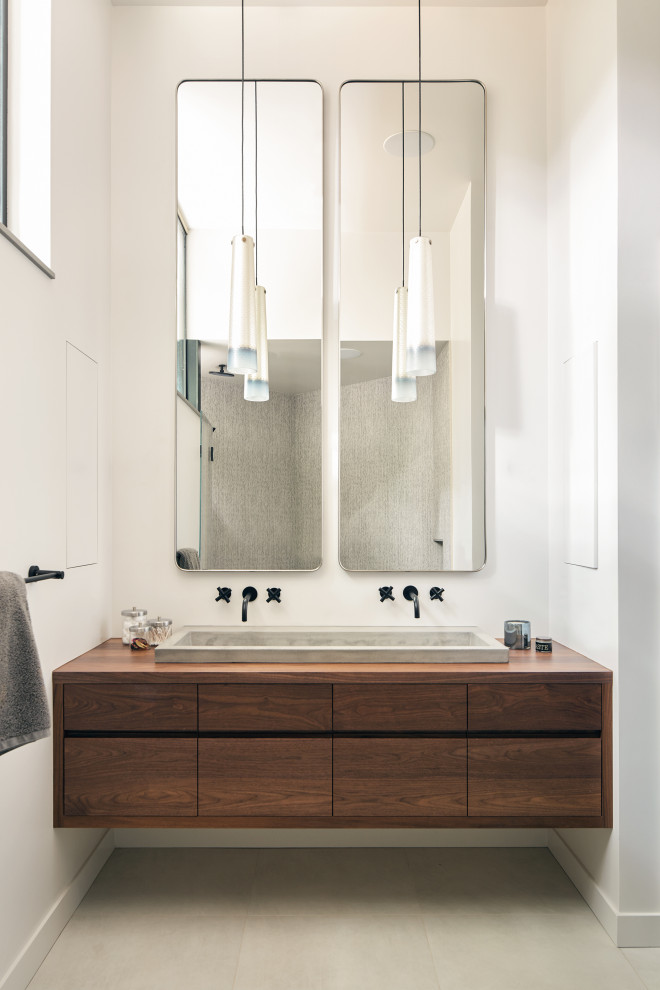 This is an example of a beach style bathroom in Sacramento with flat-panel cabinets, dark wood cabinets, a double vanity, a floating vanity, white walls, a trough sink, wood benchtops, grey floor and brown benchtops.