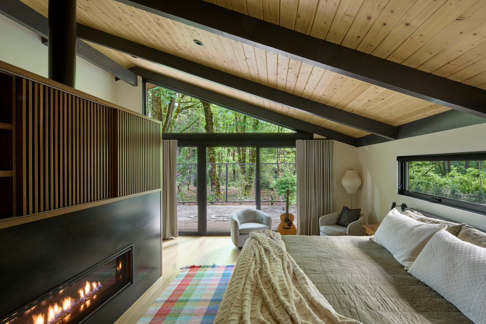 Design ideas for a midcentury master bedroom in Portland with light hardwood floors, a two-sided fireplace, a metal fireplace surround and exposed beam.