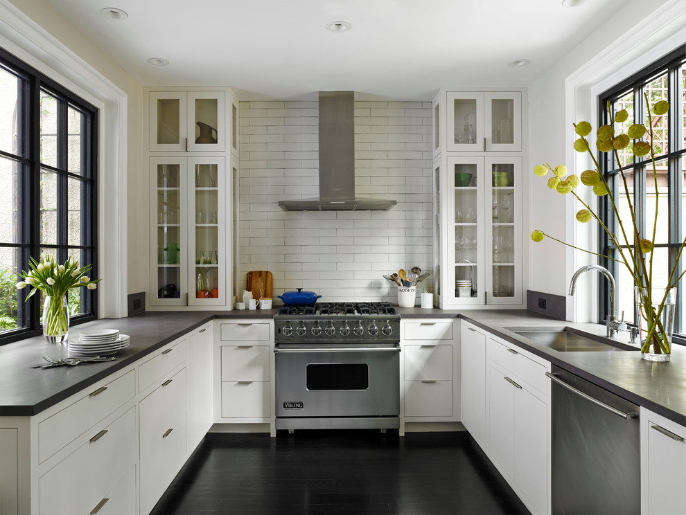 Design ideas for a transitional u-shaped separate kitchen in Philadelphia with an undermount sink, glass-front cabinets, white cabinets, white splashback, subway tile splashback, stainless steel appliances and black floor.