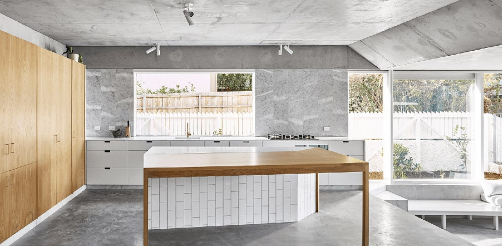 Photo of a beach style open plan kitchen in Brisbane with a single-bowl sink, flat-panel cabinets, white cabinets, grey splashback, concrete floors, with island, grey floor and grey benchtop.