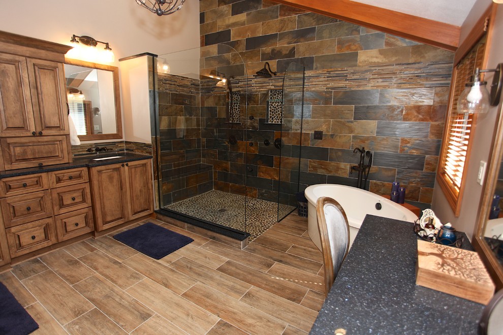 Freestanding bathtub - large rustic master slate tile brown floor freestanding bathtub idea in Indianapolis with brown cabinets, beige walls and an undermount sink