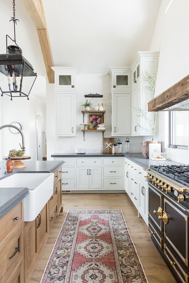 Example of a large farmhouse l-shaped dark wood floor kitchen design in Salt Lake City with white cabinets, white backsplash, black appliances, an island and gray countertops