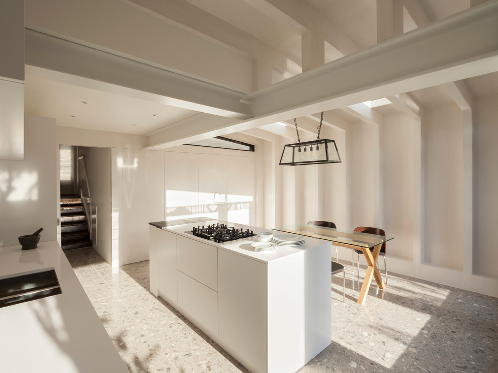 Photo of a mid-sized contemporary galley open plan kitchen in London with an integrated sink, flat-panel cabinets, white cabinets, quartz benchtops, white splashback, porcelain splashback, stainless steel appliances, terrazzo floors and with island.