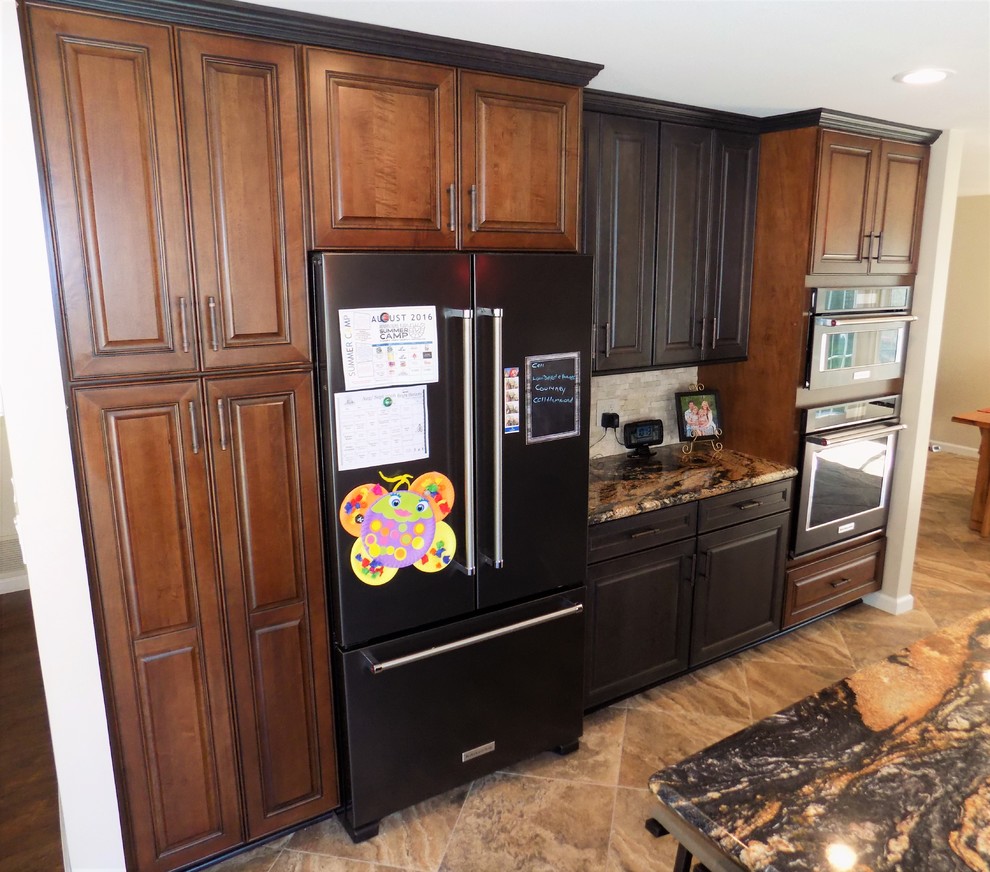 Large mediterranean l-shaped eat-in kitchen in San Diego with a farmhouse sink, raised-panel cabinets, black cabinets, granite benchtops, beige splashback, stone tile splashback, black appliances, porcelain floors and with island.