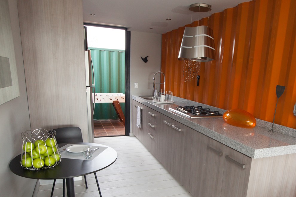 Small industrial single-wall open plan kitchen in Other with a double-bowl sink, shaker cabinets, grey cabinets, granite benchtops, orange splashback, metal splashback, stainless steel appliances, light hardwood floors and no island.