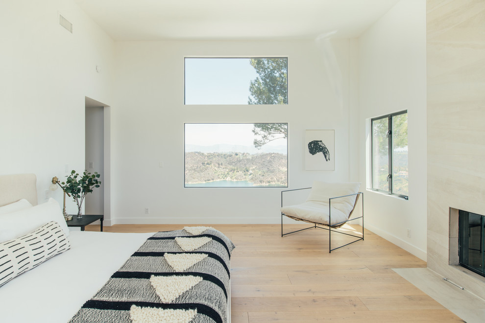 Photo of a contemporary master bedroom in Los Angeles with white walls, light hardwood floors, a standard fireplace, a stone fireplace surround and beige floor.