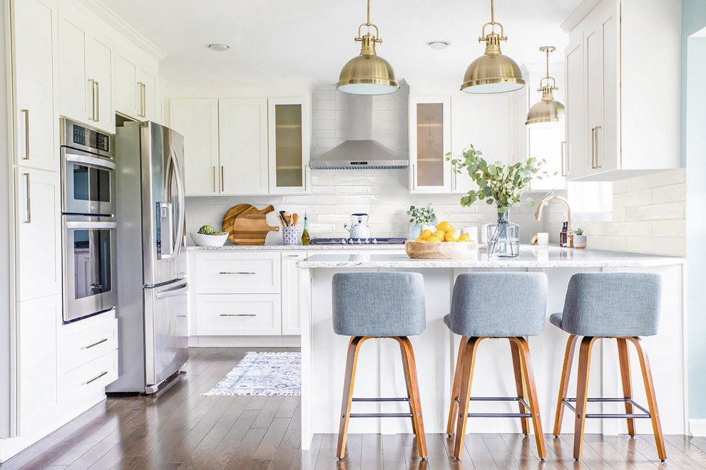 Modelo de cocinas en U contemporáneo de tamaño medio con fregadero sobremueble, armarios estilo shaker, puertas de armario blancas, encimera de cuarzo compacto, salpicadero blanco, salpicadero de azulejos tipo metro, electrodomésticos de acero inoxidable, suelo de madera en tonos medios, suelo marrón y encimeras blancas