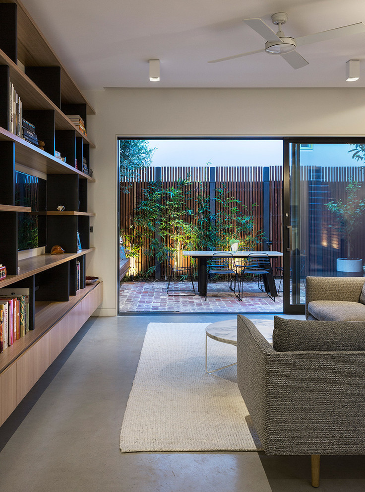 This is an example of a small modern open concept living room in Melbourne with white walls, concrete floors and a built-in media wall.