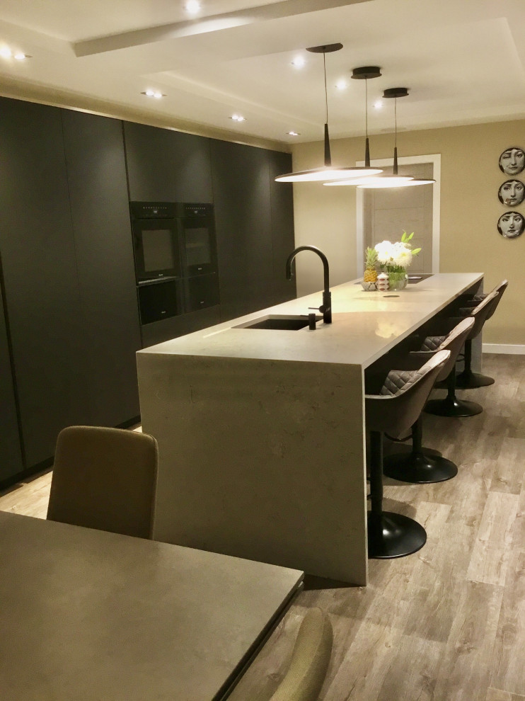 Inspiration for a medium sized contemporary cream and black galley kitchen/diner in Manchester with a submerged sink, flat-panel cabinets, black cabinets, quartz worktops, black appliances, laminate floors, an island, beige worktops and a feature wall.
