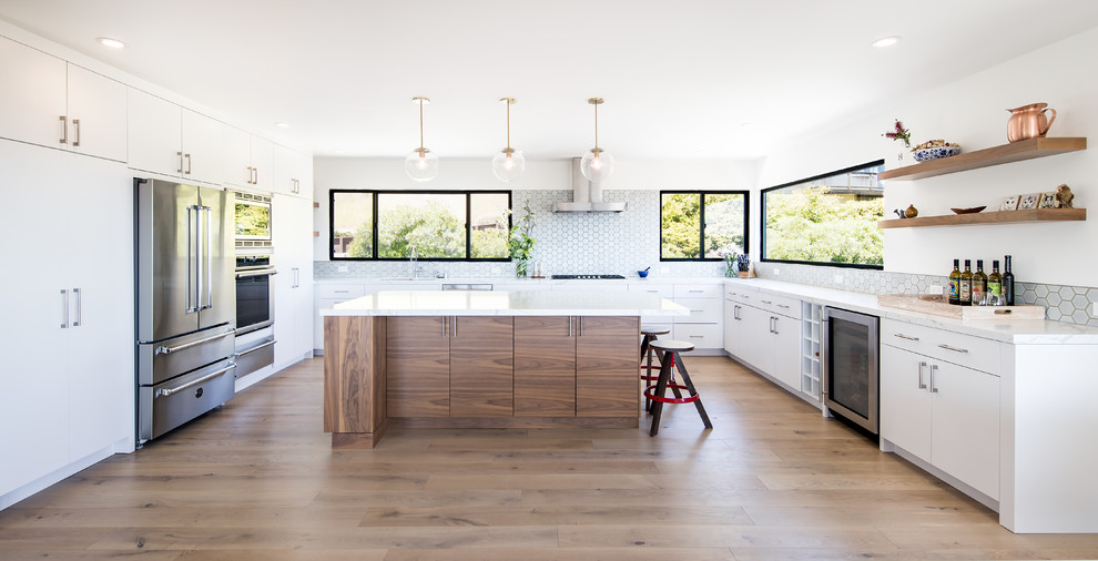 Photo of a contemporary u-shaped kitchen in San Francisco with an undermount sink, flat-panel cabinets, white cabinets, white splashback, mosaic tile splashback, stainless steel appliances, light hardwood floors, with island, beige floor and white benchtop.