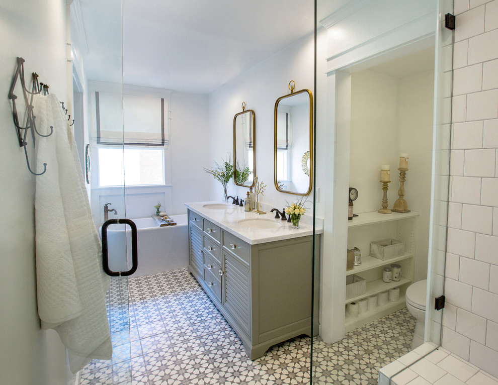 Photo of a mid-sized country master bathroom in Los Angeles with louvered cabinets, grey cabinets, a freestanding tub, an alcove shower, a one-piece toilet, white tile, ceramic tile, white walls, cement tiles, an undermount sink, marble benchtops, grey floor and a hinged shower door.