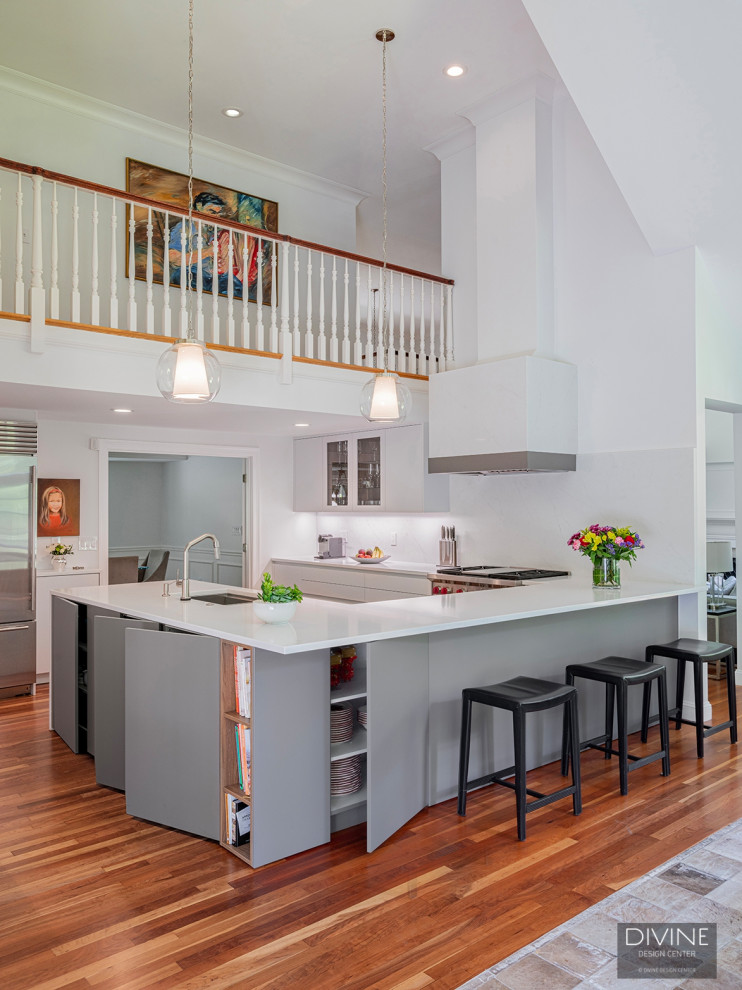 Photo of a mid-sized modern u-shaped eat-in kitchen in Boston with an undermount sink, flat-panel cabinets, white cabinets, white splashback, stainless steel appliances, medium hardwood floors, a peninsula, brown floor, white benchtop and vaulted.