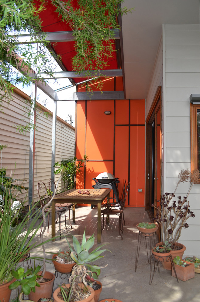 This is an example of a mid-sized eclectic one-storey orange house exterior in Melbourne with concrete fiberboard siding, a flat roof, a metal roof, a grey roof and clapboard siding.