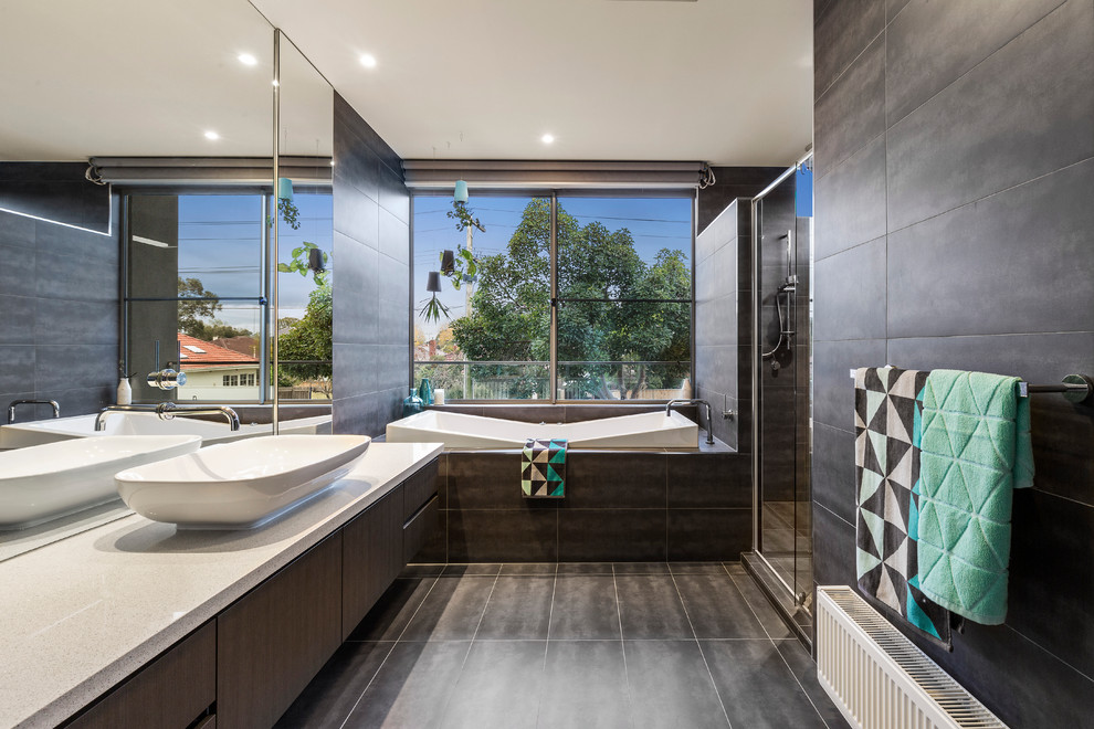 Design ideas for a contemporary bathroom in Melbourne with flat-panel cabinets, dark wood cabinets, a drop-in tub, black tile, black walls, a vessel sink and grey benchtops.
