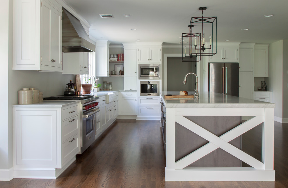 Inspiration for a large transitional l-shaped dark wood floor enclosed kitchen remodel in Newark with a farmhouse sink, shaker cabinets, white cabinets, marble countertops, white backsplash, stainless steel appliances and an island