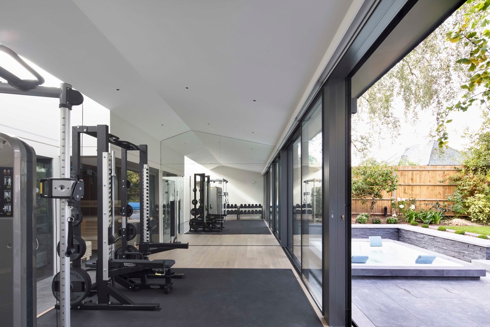 Photo of a mid-sized contemporary multipurpose gym in London with white walls, light hardwood floors and beige floor.