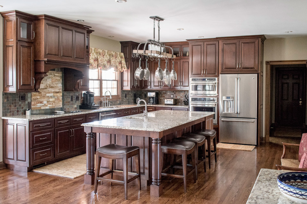 Large traditional l-shaped eat-in kitchen in Louisville with an undermount sink, raised-panel cabinets, dark wood cabinets, granite benchtops, multi-coloured splashback, slate splashback, stainless steel appliances, medium hardwood floors, with island, brown floor and multi-coloured benchtop.