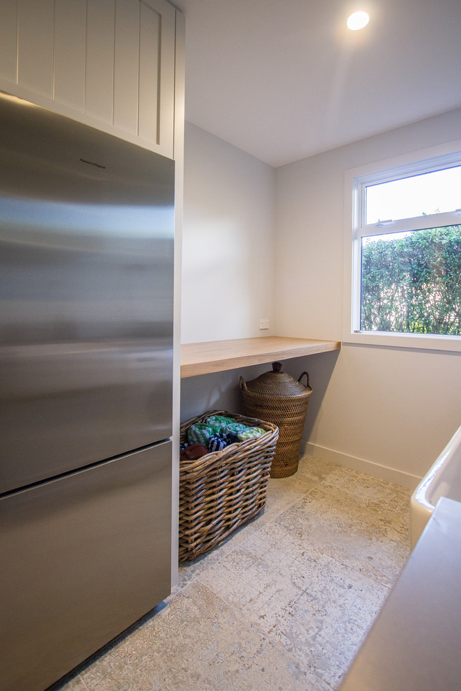 Photo of a small traditional galley utility room in Napier-Hastings with a farmhouse sink, recessed-panel cabinets, white cabinets, quartz benchtops, white walls, ceramic floors, a side-by-side washer and dryer, multi-coloured floor and grey benchtop.