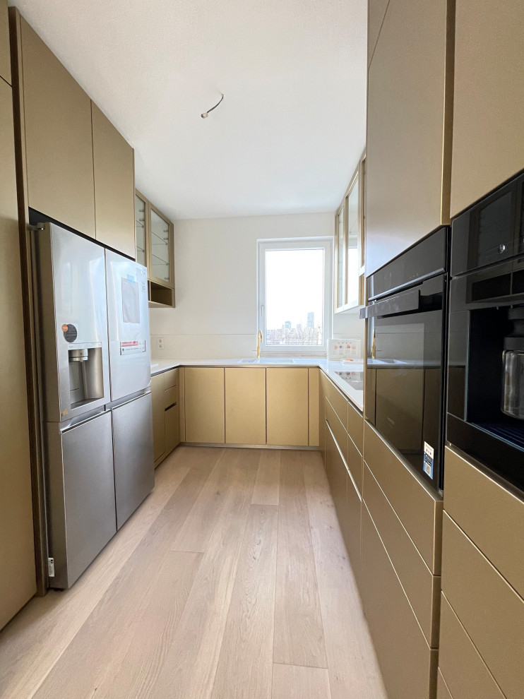 Large contemporary u-shaped separate kitchen in Berlin with a double-bowl sink, flat-panel cabinets, beige cabinets, solid surface benchtops, white splashback, ceramic splashback, black appliances, painted wood floors, no island, beige floor, white benchtop and recessed.