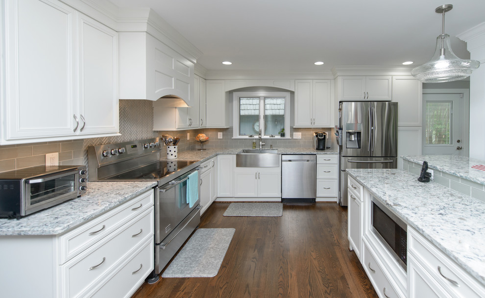 Large transitional l-shaped dark wood floor and brown floor kitchen photo in Baltimore with a farmhouse sink, recessed-panel cabinets, white cabinets, quartz countertops, gray backsplash, subway tile backsplash, stainless steel appliances and an island