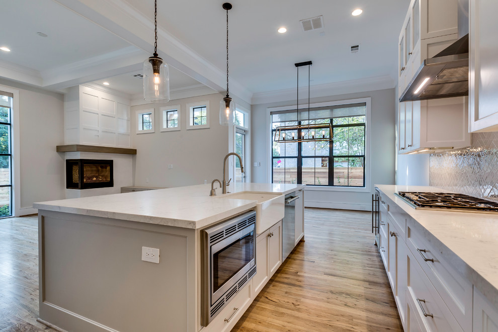 Eat-in kitchen - mid-sized transitional open concept and l-shaped light wood floor eat-in kitchen idea in Houston with white walls, a corner fireplace, a media wall, an undermount sink, shaker cabinets, white cabinets, gray backsplash, subway tile backsplash, stainless steel appliances, an island and white countertops