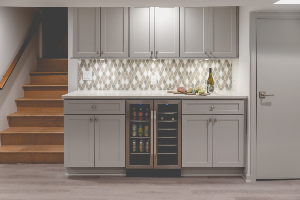 This is an example of a mid-sized transitional single-wall home bar in Chicago with shaker cabinets, grey cabinets, quartz benchtops, multi-coloured splashback, mosaic tile splashback, vinyl floors, grey floor and white benchtop.