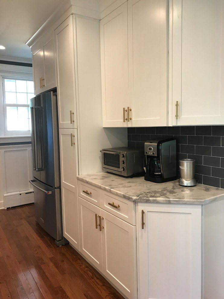 Example of a mid-sized transitional l-shaped light wood floor and brown floor kitchen design in Philadelphia with an undermount sink, recessed-panel cabinets, white cabinets, quartzite countertops, gray backsplash, glass tile backsplash, stainless steel appliances and a peninsula