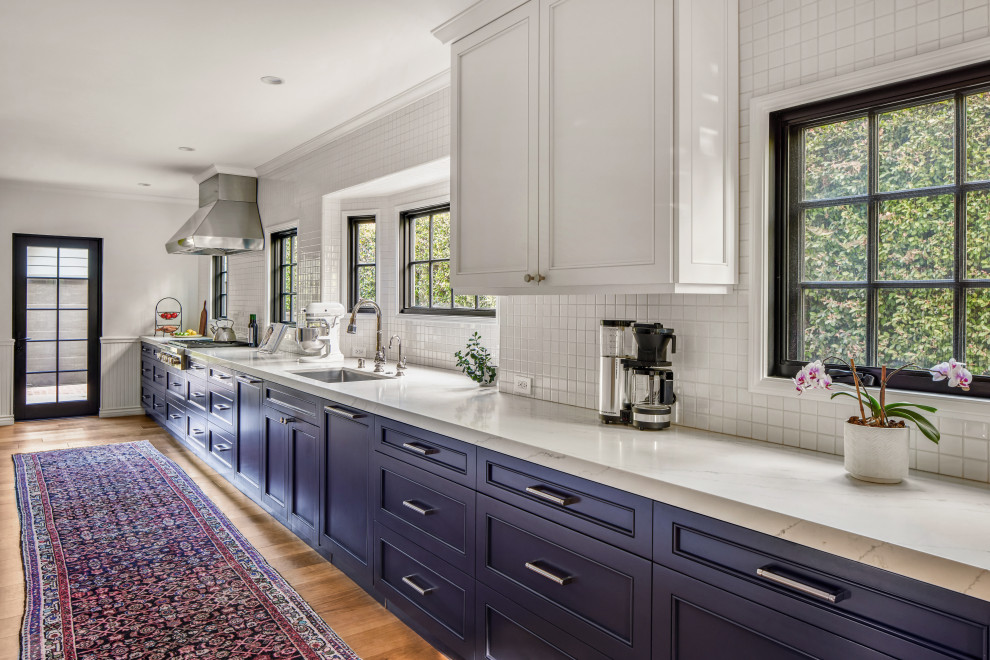 Inspiration for a mid-sized timeless medium tone wood floor and beige floor eat-in kitchen remodel in Los Angeles with shaker cabinets, blue cabinets, solid surface countertops, white backsplash, mosaic tile backsplash, stainless steel appliances, a peninsula, white countertops and a single-bowl sink