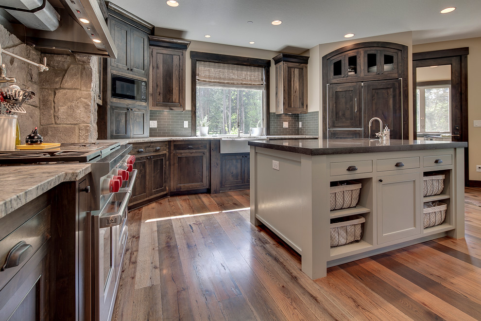 Design ideas for a large country l-shaped open plan kitchen in Portland with a farmhouse sink, recessed-panel cabinets, dark wood cabinets, granite benchtops, brown splashback, glass tile splashback, stainless steel appliances, medium hardwood floors and with island.