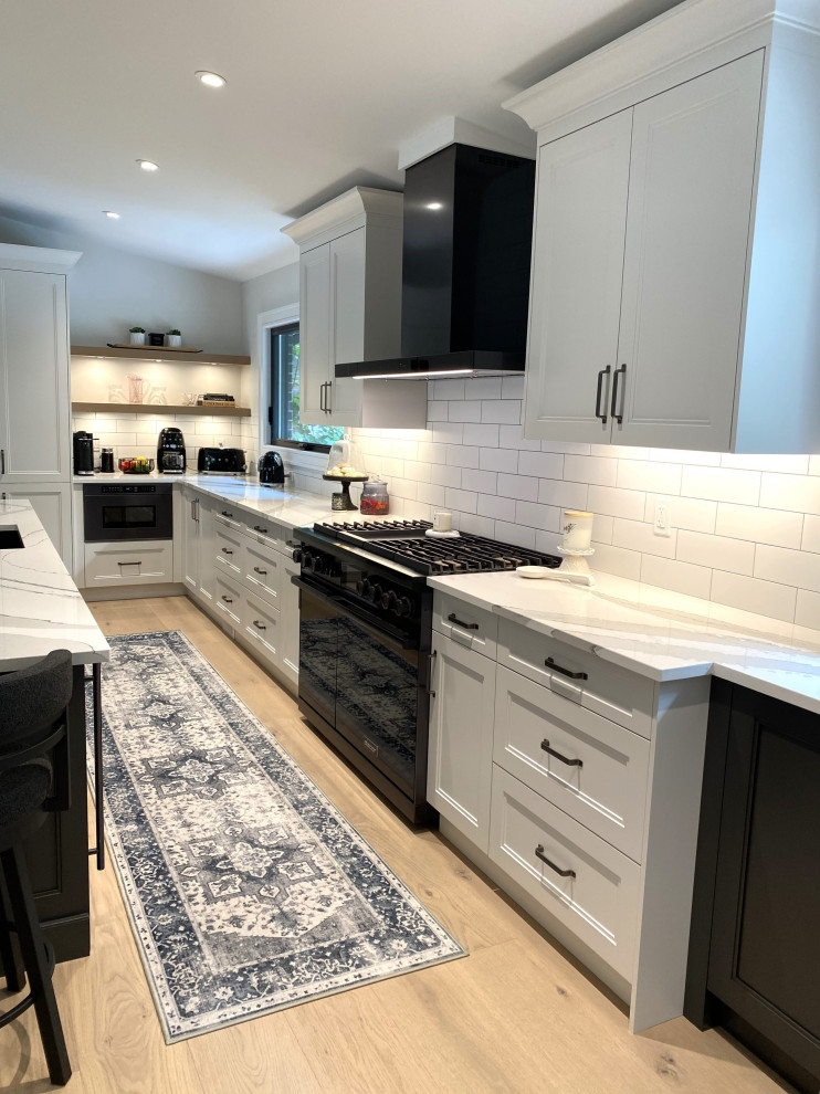 Large transitional l-shaped light wood floor and vaulted ceiling open concept kitchen photo in Toronto with an undermount sink, recessed-panel cabinets, white cabinets, quartz countertops, white backsplash, porcelain backsplash, stainless steel appliances, an island and white countertops